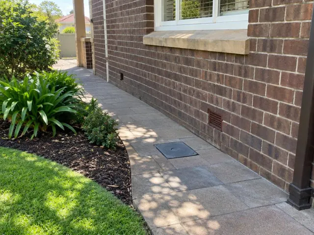 Brick side wall with tiled path and a flush capped access cover, tidy garden border in Gladesville